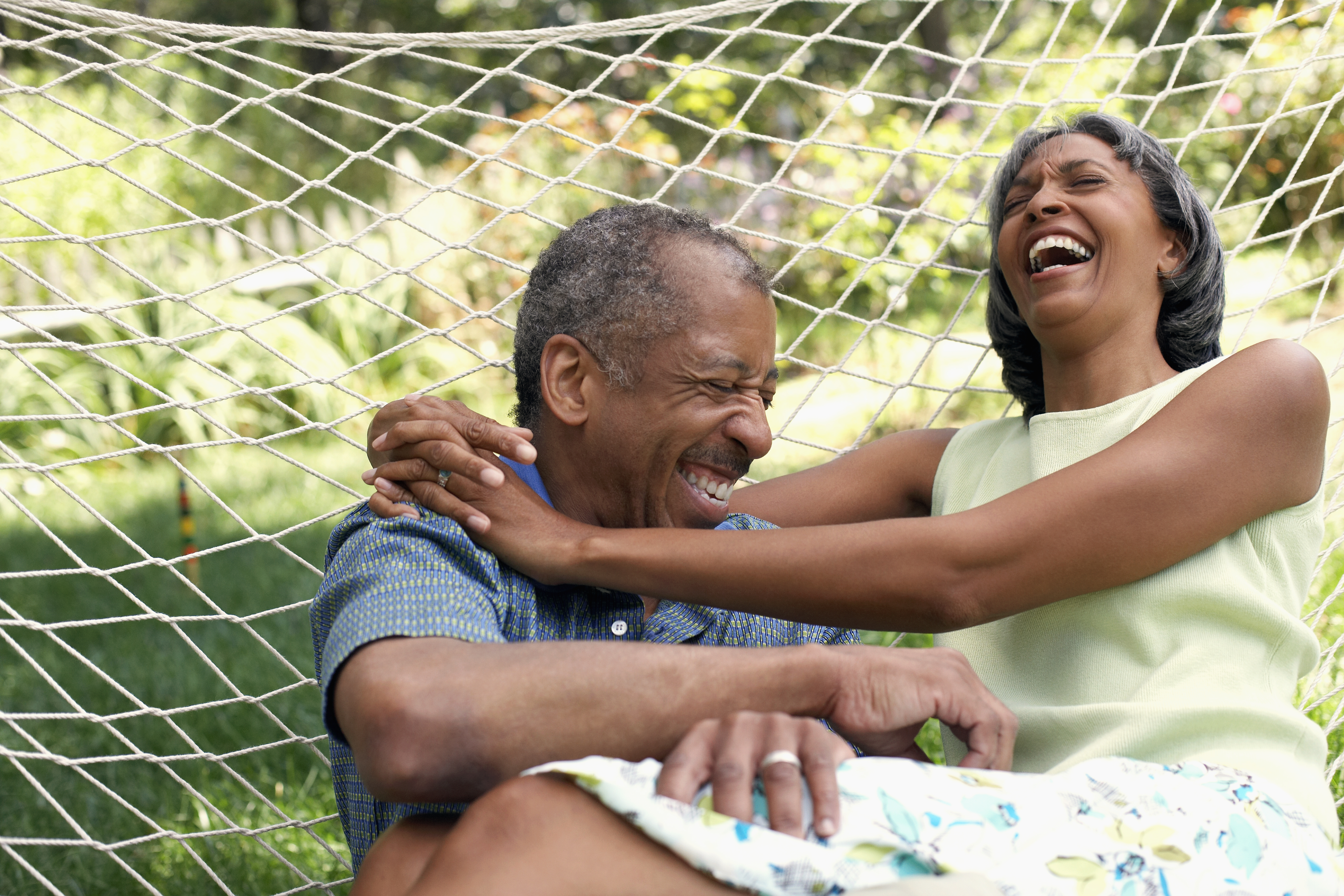 An older couple hugging and laughing in a hammock.